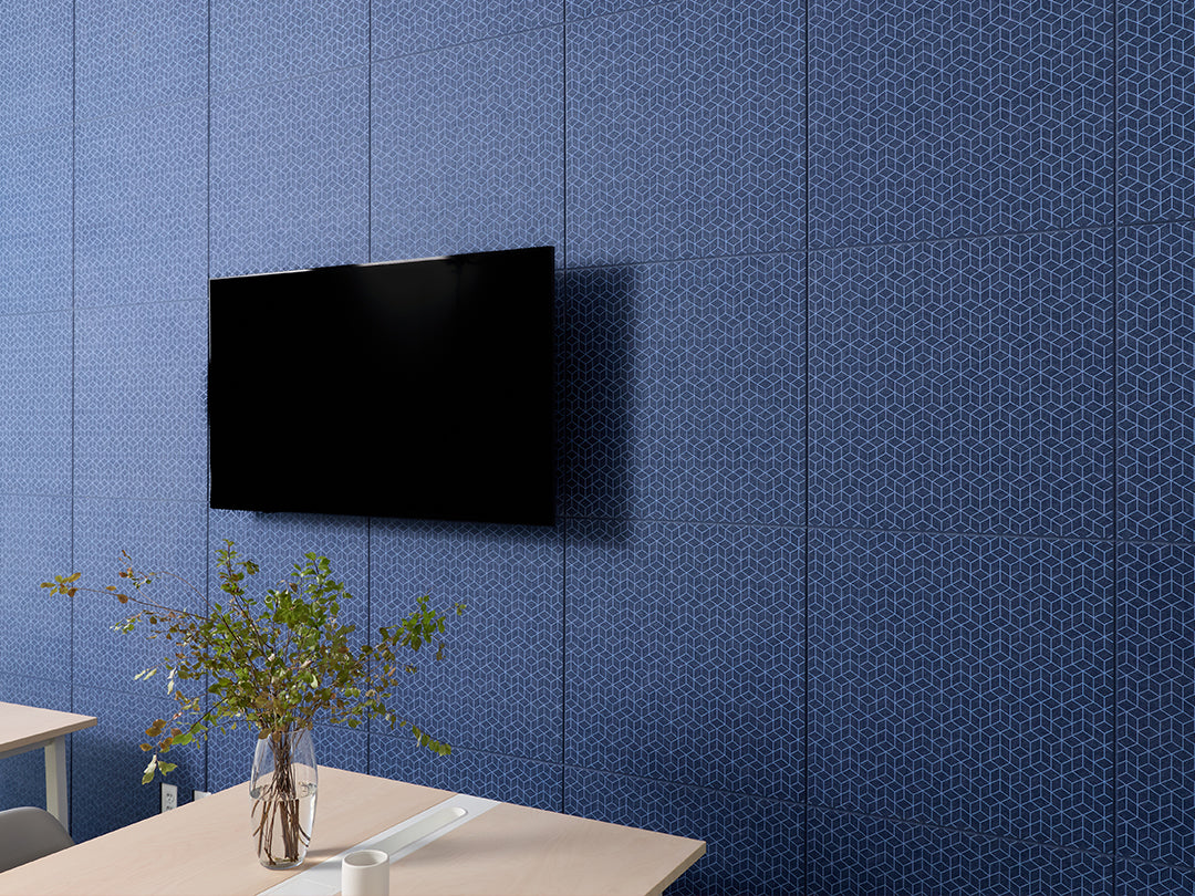 Black flat-screen TV mounted on a blue patterned wall with a table and plant in the foreground.