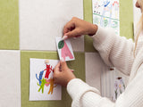 Person hanging children's artwork on a tiled wall