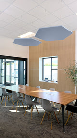 Two blue-gray hexagonal acoustic baffles suspended from ceiling in modern office conference room.