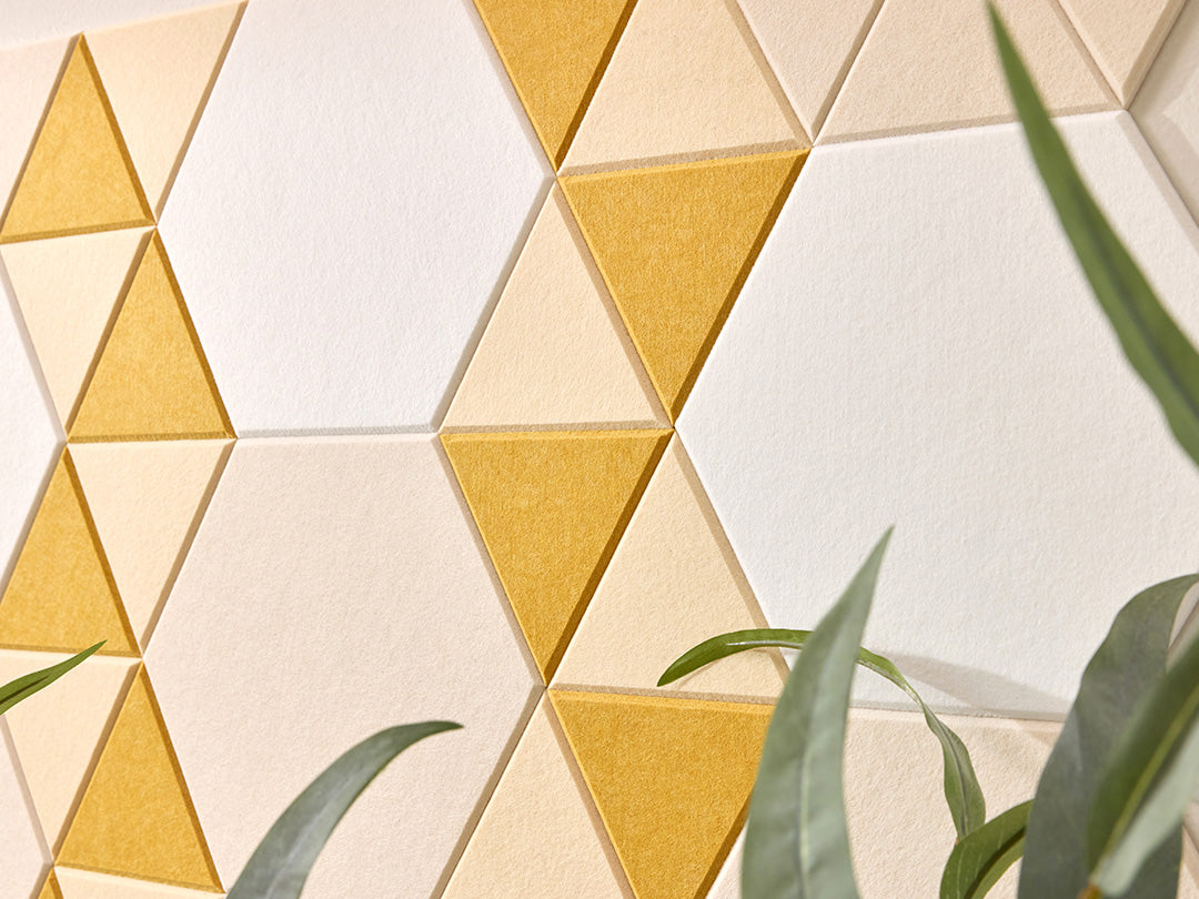 Geometric triangle-patterned wall with yellow and beige tiles, partially obscured by green leaves.