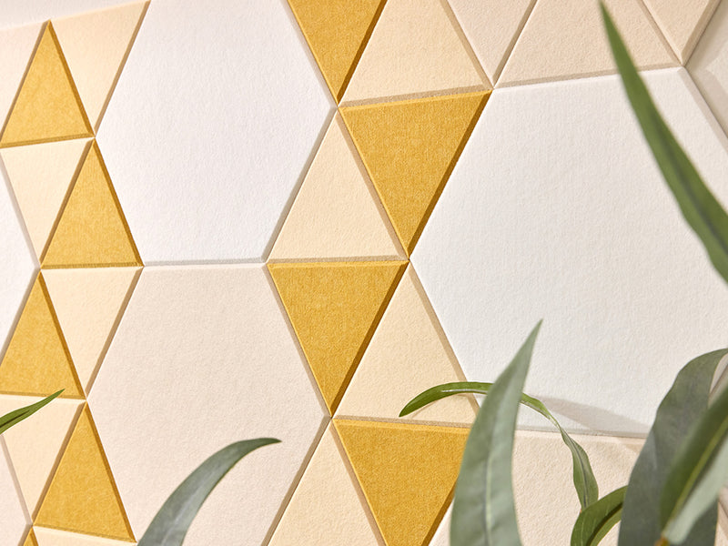 Geometric triangle-patterned wall with yellow and beige tiles, partially obscured by green leaves.