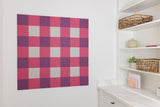 Checkered acoustic wall panel in pink, purple, and gray on a white wall with shelves below.