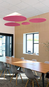 Four pink oval acoustic baffles suspended from ceiling above conference table in modern office space.