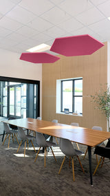Two burgundy hexagonal acoustic panels suspended from ceiling above conference table in office space.