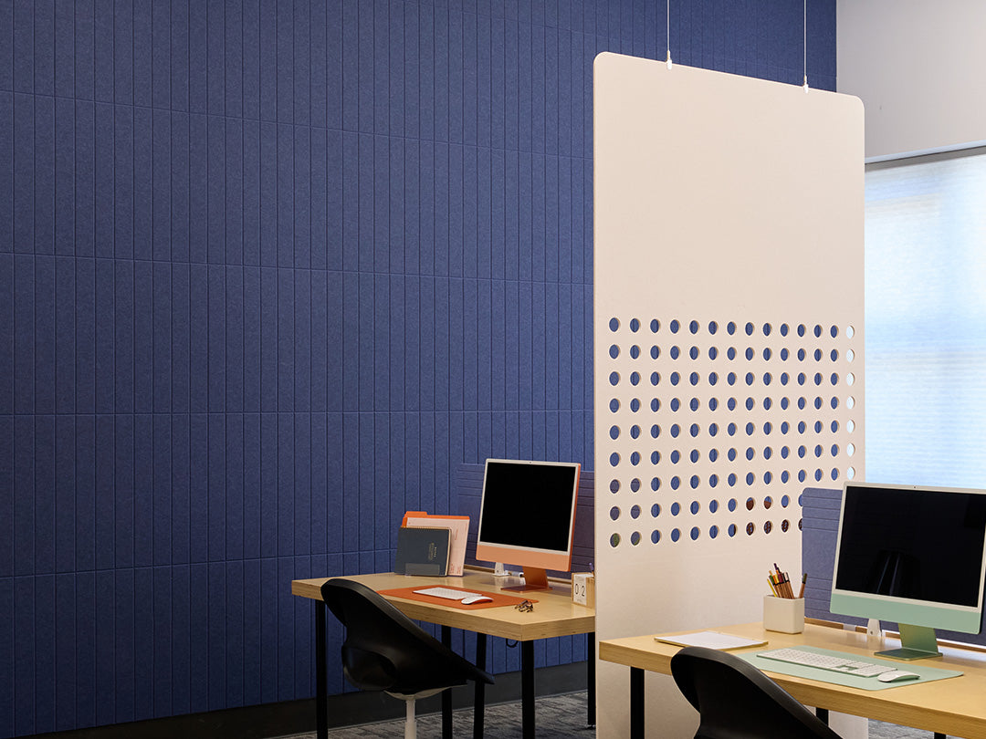 Modern office setup with a blue wall, white partition, and two desks with computers.