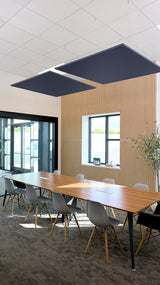 Two dark blue square flat acoustic panels suspended from ceiling grid above conference table in office space.