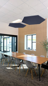 Two dark blue hexagonal acoustic baffles suspended from ceiling in modern office meeting room.