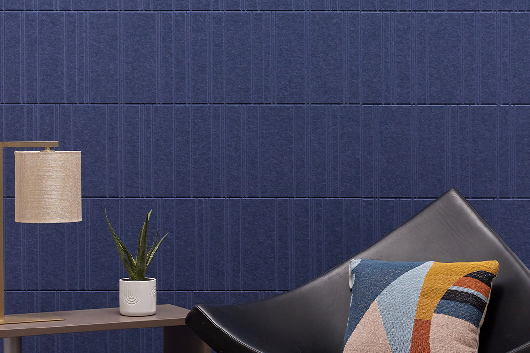 Modern interior with a blue textured acoustic wall, black chair, and decorative pillow.