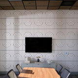 A modern conference room featuring a large wall-mounted black television in front of a white wall with a repeating black geometric oval pattern. Below the TV is a light gray console table with decorative items, and in the foreground is a wooden conference table surrounded by gray chairs.