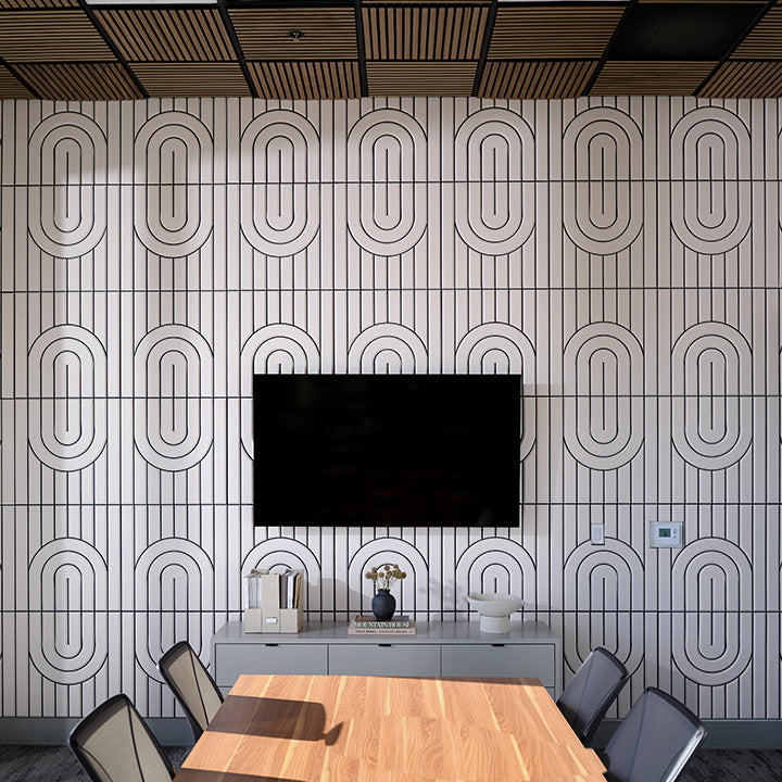 A modern conference room featuring a large wall-mounted black television in front of a white wall with a repeating black geometric oval pattern. Below the TV is a light gray console table with decorative items, and in the foreground is a wooden conference table surrounded by gray chairs.
