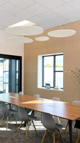 Multiple beige flat circular acoustic baffles suspended from ceiling above conference table in office space.