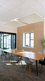 Two large square cream-colored acoustic panels suspended from ceiling in modern office conference room above wooden table.