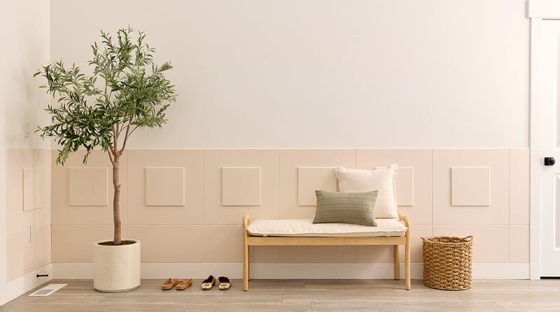 Wainscoting in a nook with a plant, bench, and shoes on a wooden floor.