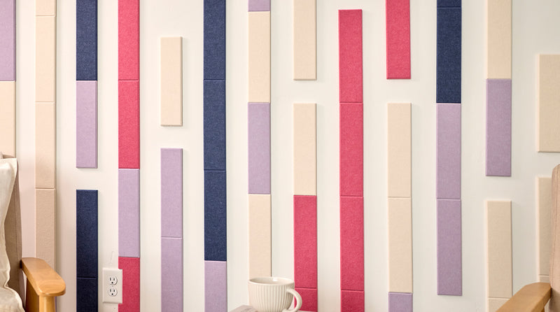 Two beige armchairs in a room with a decorative wall featuring vertical color acoustic tiles.