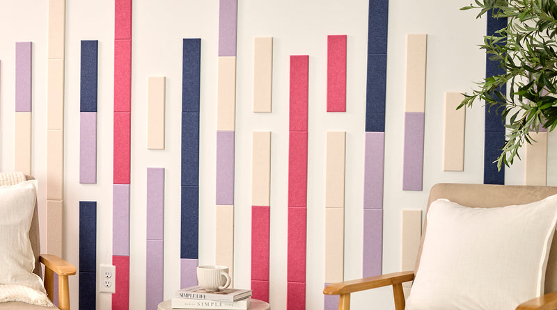 Two beige armchairs in a room with a decorative wall featuring vertical color acoustic tiles.