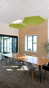 Two lime green hexagonal acoustic baffles suspended from ceiling in modern office conference room.