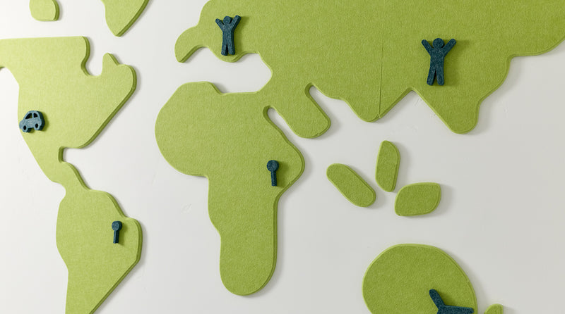 Green acoustic felt cutout world map with small figures on a white background