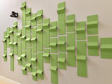 Green dimensional tiles arranged in varied heights and depths on a beige wall, creating a textured geometric pattern.