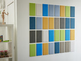 A Felt Right Wall Art design in shades of blue green grey white and yellow felt tiles next to a shelf.