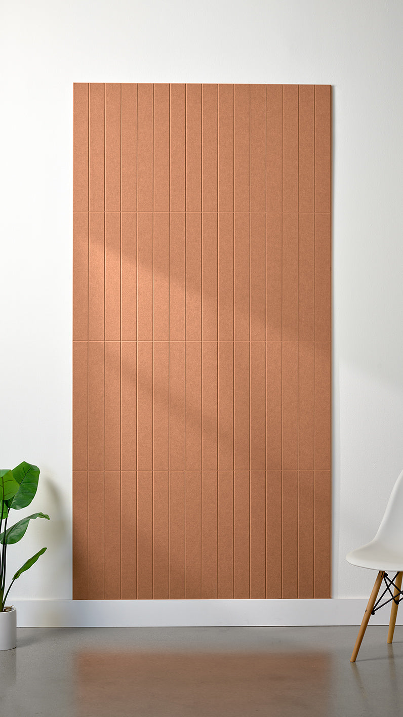 Light orange Felt Right 4’ x 8’ PET felt panel with straight vertical lines engraved into the material against a white wall. A plant and chair are in the foreground.