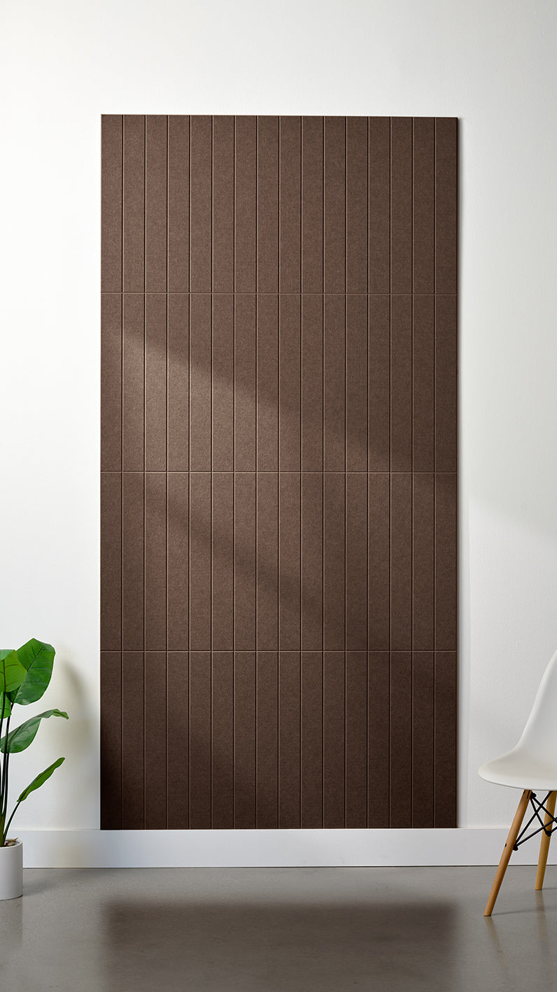 Brown Felt Right 4’ x 8’ PET felt panel with straight vertical lines engraved into the material against a white wall. A plant and chair are in the foreground.