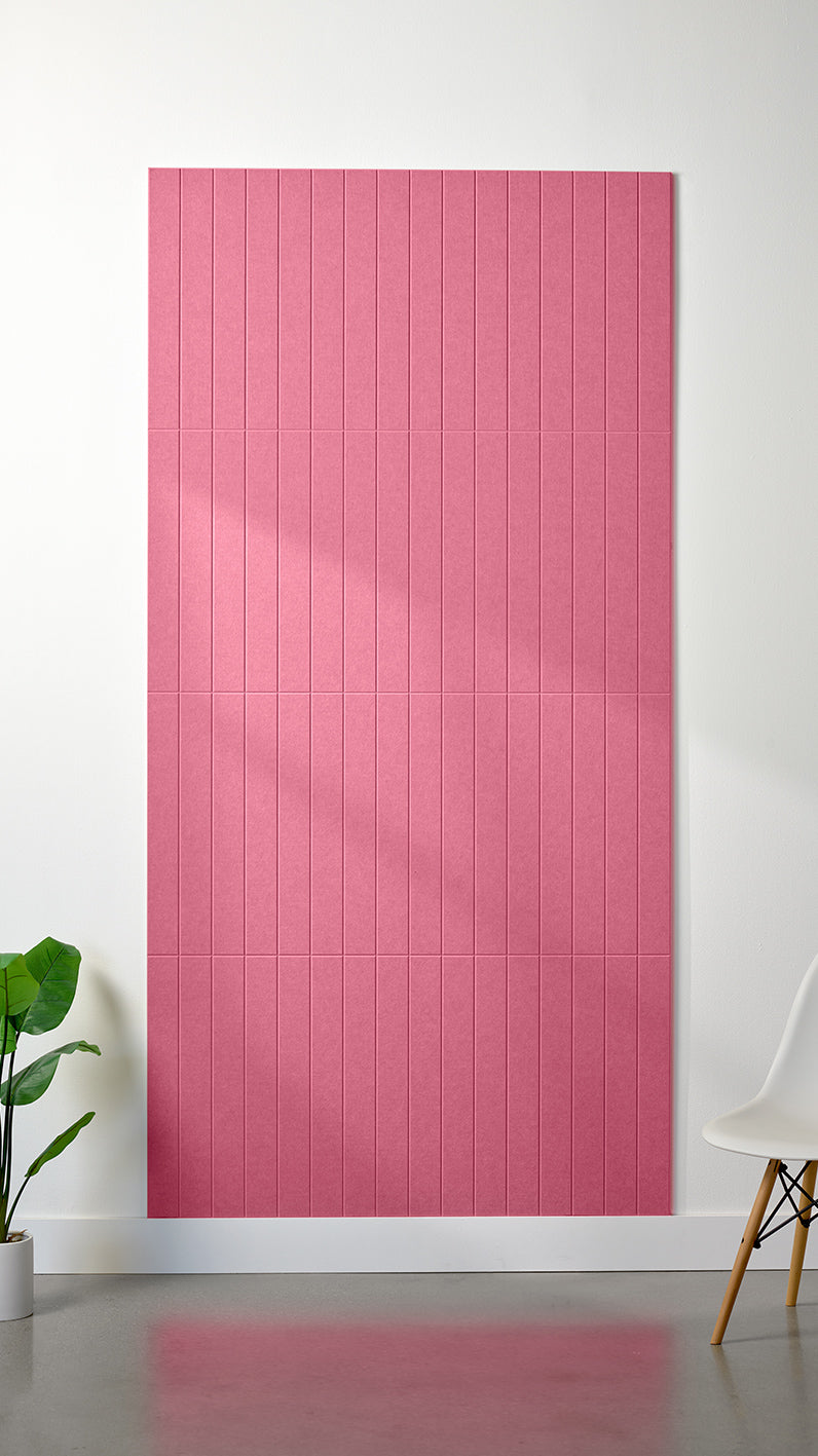 Hot pink Felt Right 4’ x 8’ PET felt panel with straight vertical lines engraved into the material against a white wall. A plant and chair are in the foreground.