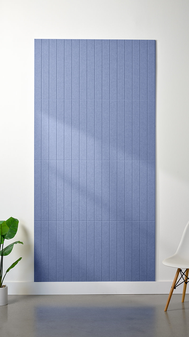 Periwinkle Felt Right 4’ x 8’ PET felt panel with straight vertical lines engraved into the material against a white wall. A plant and chair are in the foreground.