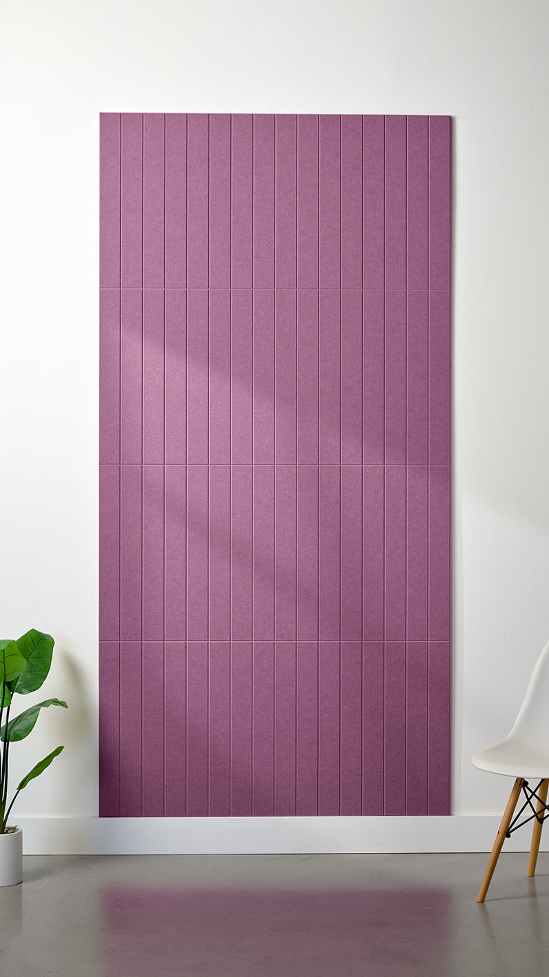 Light purple Felt Right 4’ x 8’ PET felt panel with straight vertical lines engraved into the material against a white wall. A plant and chair are in the foreground.