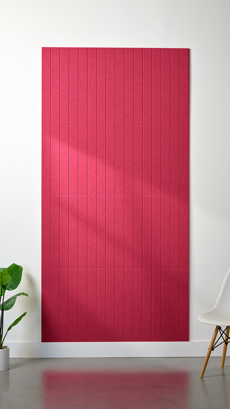 Bright red Felt Right 4’ x 8’ PET felt panel with straight vertical lines engraved into the material against a white wall. A plant and chair are in the foreground.