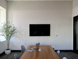 Modern conference room with wooden table, gray chairs, wall-mounted black screen, and potted plant.