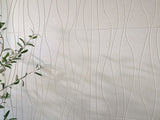 Beige ceramic tile with wavy linear pattern and green plant foliage visible on left edge.
