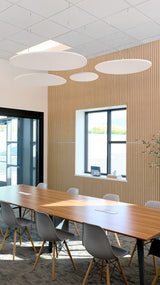 Three pebble-colored flat circular acoustic baffles suspended from ceiling above conference table.