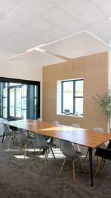 Two white square acoustic panels suspended from ceiling in modern office meeting room above wooden table.