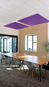 Two purple square acoustic ceiling baffles suspended above a conference table in an office space.