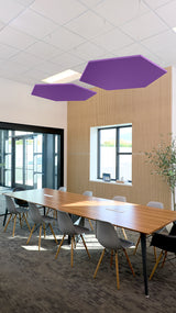 Two purple hexagonal acoustic baffles suspended from ceiling above conference table in office space.