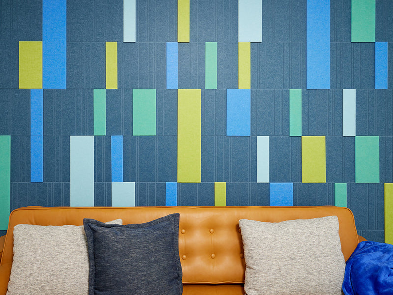 A Felt Right wall art design in shades of blue and green creating a geometric design covering a wall in a room with a couch and decorative pillows.