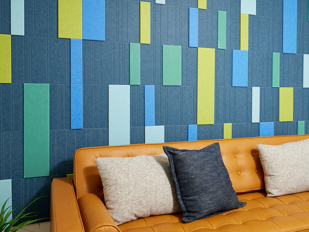 A Felt Right wall art design in shades of blue and green creating a geometric design covering a wall in a room with a couch and decorative pillows.