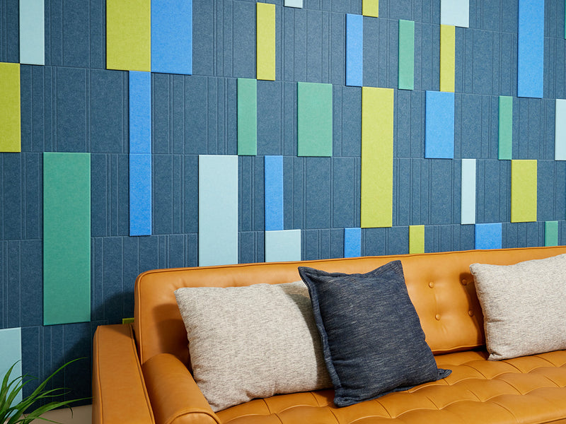 A Felt Right wall art design in shades of blue and green creating a geometric design covering a wall in a room with a couch and decorative pillows.