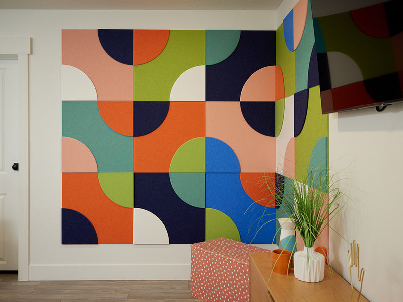 Colorful acoustic wall art in a room with a wooden side table and plant.