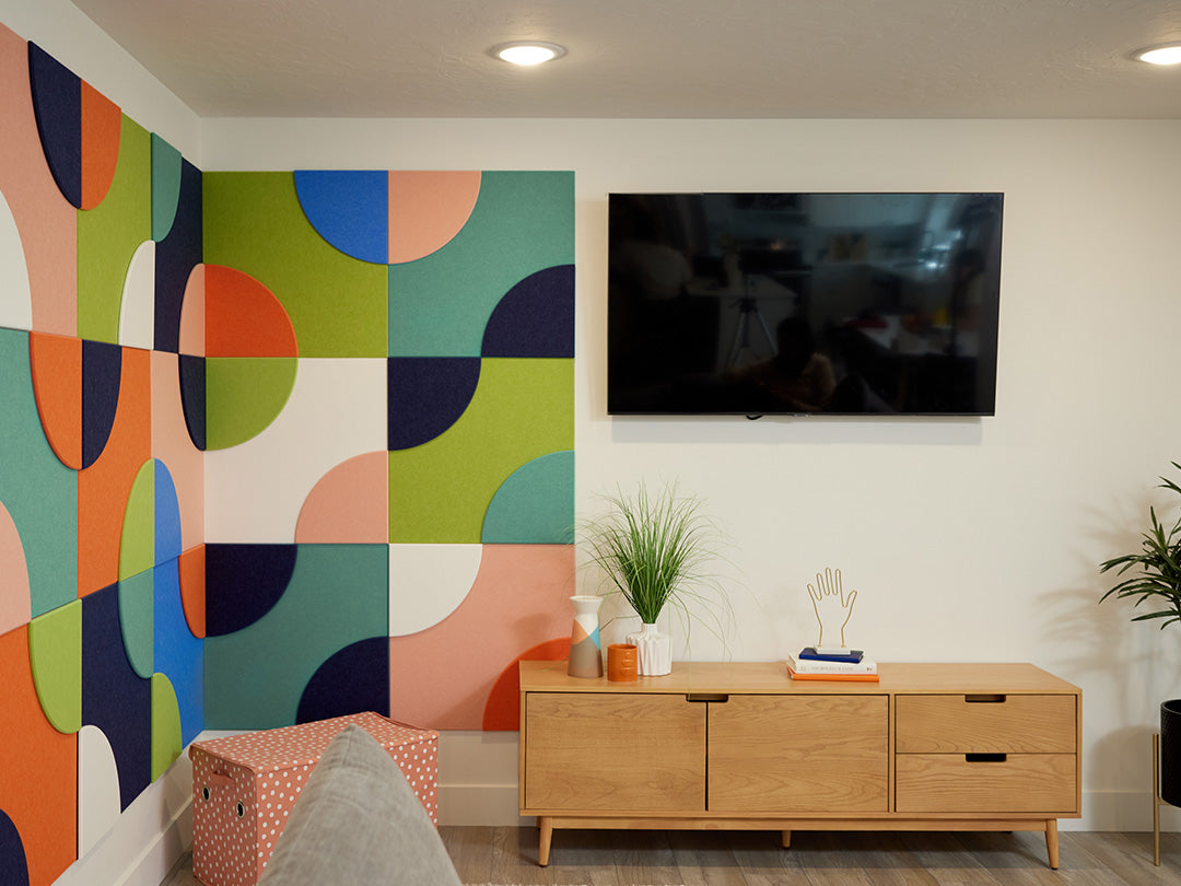 Modern living room with colorful acoustic wall design, TV, and wooden cabinet.