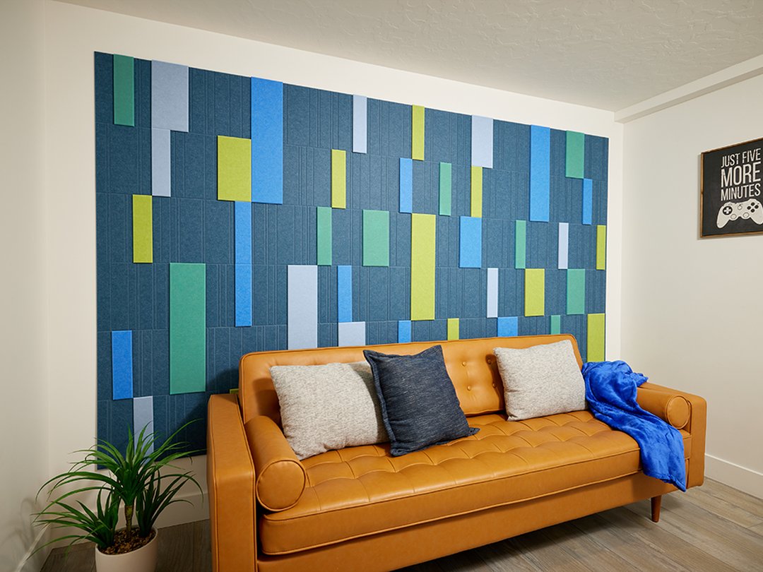A Felt Right wall art design in shades of blue and green creating a geometric design covering a wall in a room with a couch and decorative pillows.