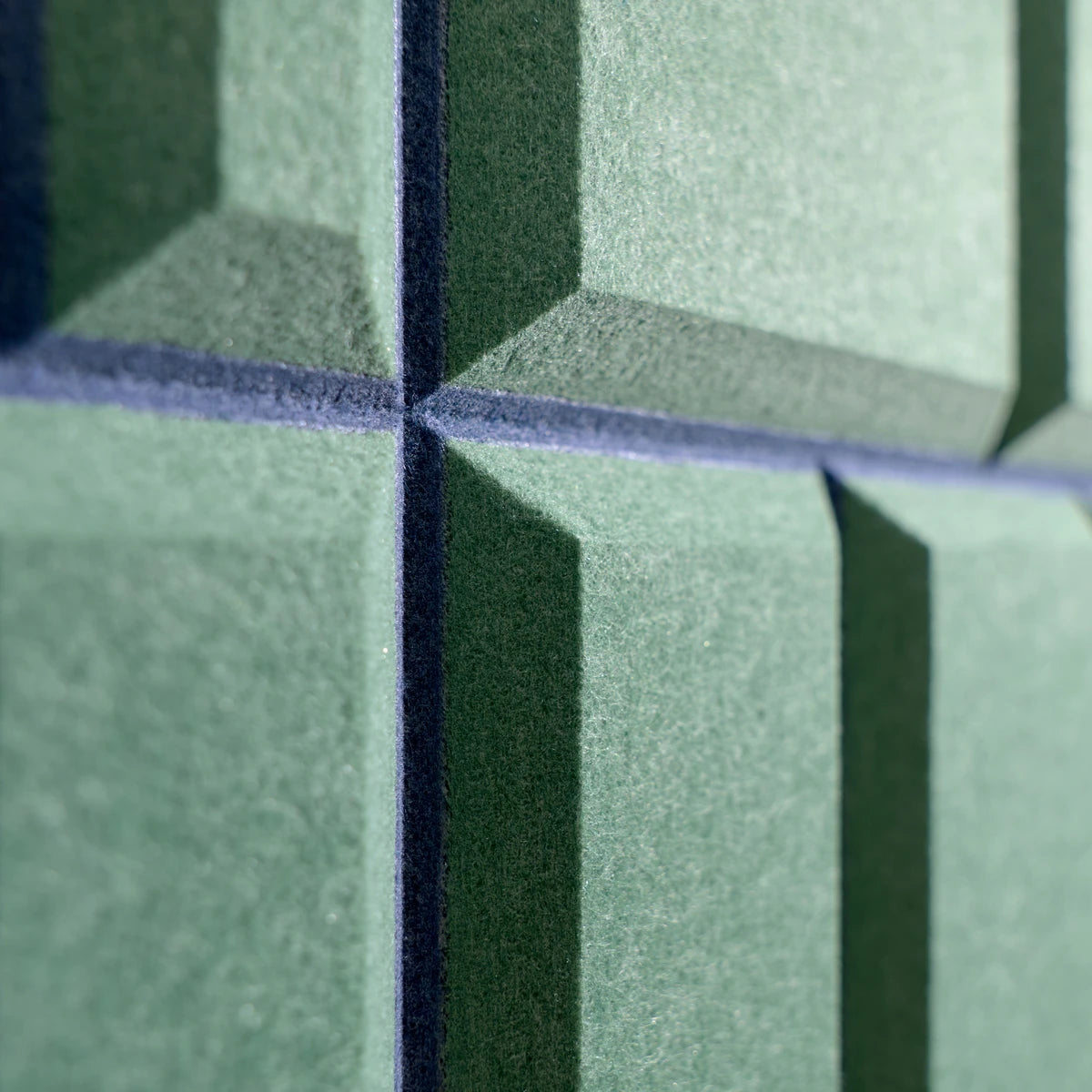 Close-up of green acoustic felt panels with a textured surface and dark blue-gray grout lines forming a geometric pattern.