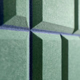 Close-up of green acoustic felt panels with a textured surface and dark blue-gray grout lines forming a geometric pattern.