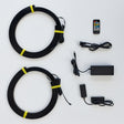 Black coiled cable kit with two large loops secured by yellow bands, shown with a remote control, power adapter, and small push-button controller on a white background.