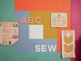 Felt Right square tiles in shades of green, blue, yellow, orange, and pink in a quilt pattern called log cabin and the felt is pinable with some fabric and letters.