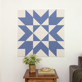 Blue and white geometric wall art on a white wall with a wooden side table and plant below.