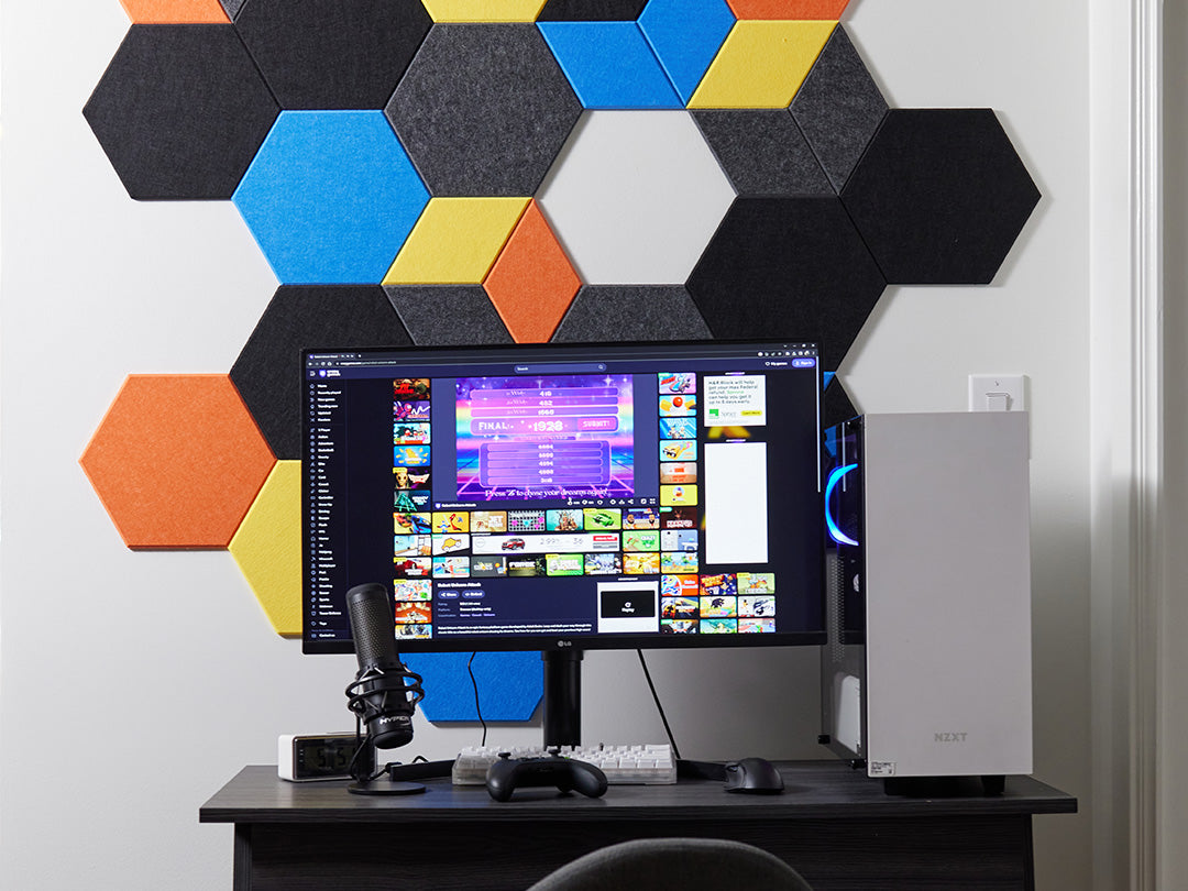 Computer setup with a monitor, keyboard, and mouse on a desk against a colorful hexagonal wall panel.