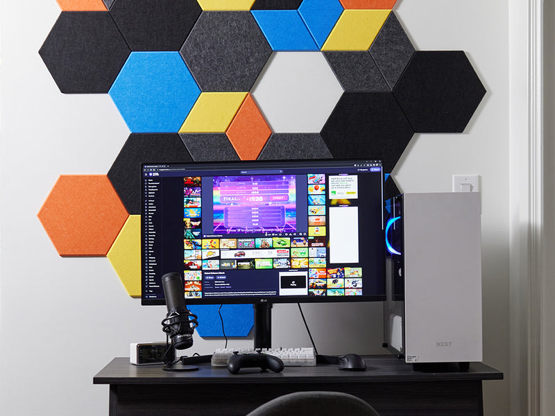 Computer setup with a monitor, keyboard, and mouse on a desk against a colorful hexagonal wall panel.