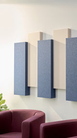 Three rectangular acoustic panels in blue and cream mounted on a white wall above a burgundy chair.