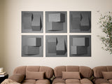 Six gray dimensional tiles with geometric shapes and shadow effects arranged in a grid on a wall above a tan sectional sofa.